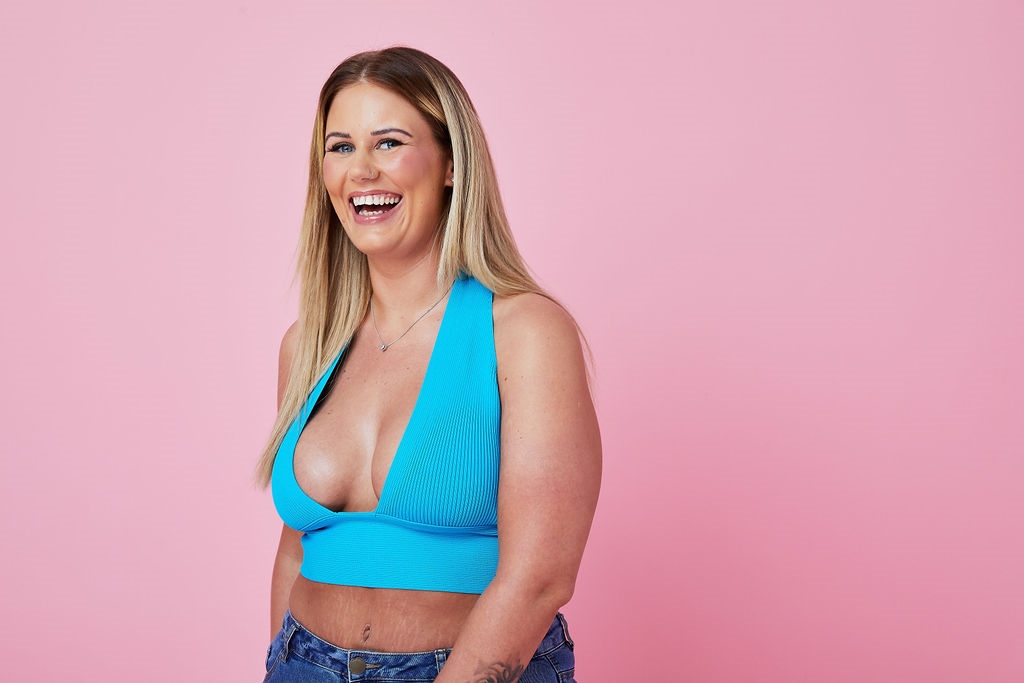 Woman in blue top smiling stood against pink background Woman in blue top smiling stood against pink background